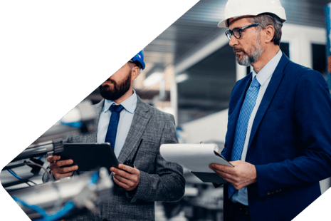 Two men in suits and hardhats with clipboards