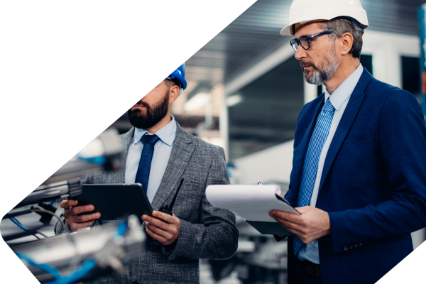Two men in suits and hardhats with clipboards